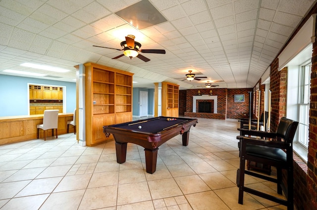 rec room featuring ceiling fan, billiards, a brick fireplace, light tile patterned floors, and brick wall