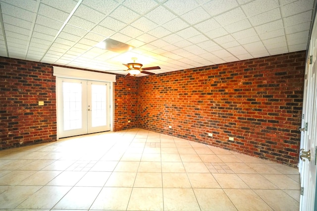 unfurnished room with ceiling fan, brick wall, a paneled ceiling, and french doors