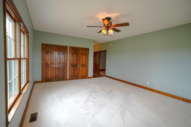 unfurnished bedroom featuring ceiling fan, multiple closets, and carpet