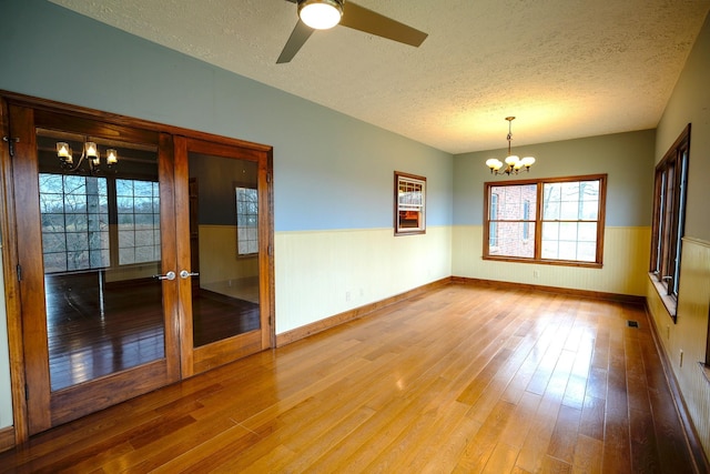 empty room featuring wood-type flooring, wooden walls, ceiling fan with notable chandelier, and a textured ceiling