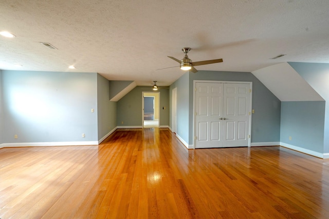 additional living space featuring ceiling fan, a textured ceiling, hardwood / wood-style flooring, and vaulted ceiling