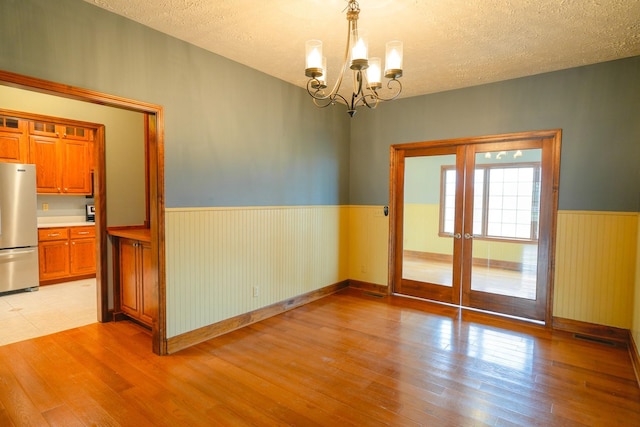 unfurnished room featuring light wood-type flooring, a textured ceiling, and a notable chandelier