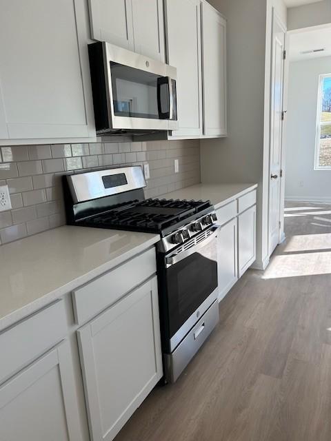 kitchen with white cabinets, backsplash, stainless steel appliances, and light hardwood / wood-style flooring