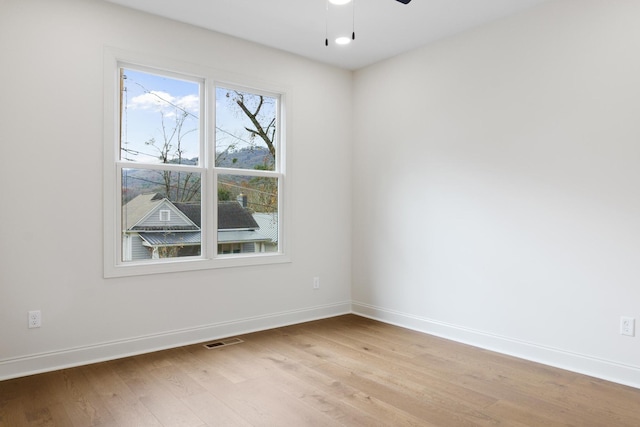 spare room featuring light wood-type flooring, visible vents, ceiling fan, and baseboards