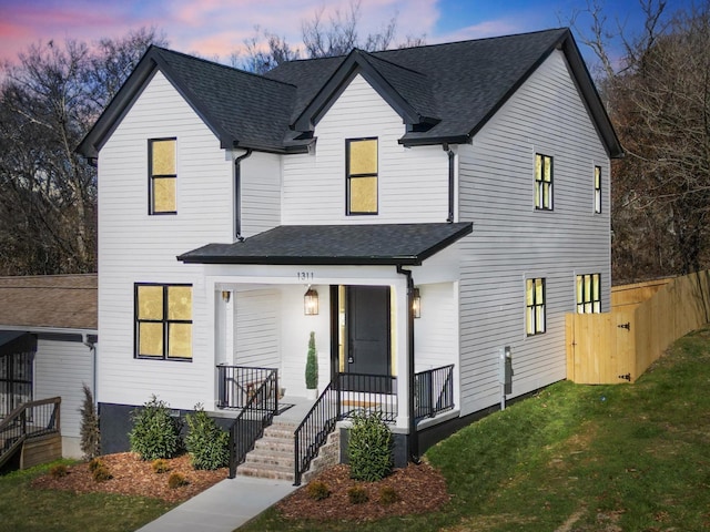 modern inspired farmhouse featuring covered porch, a shingled roof, and a front yard