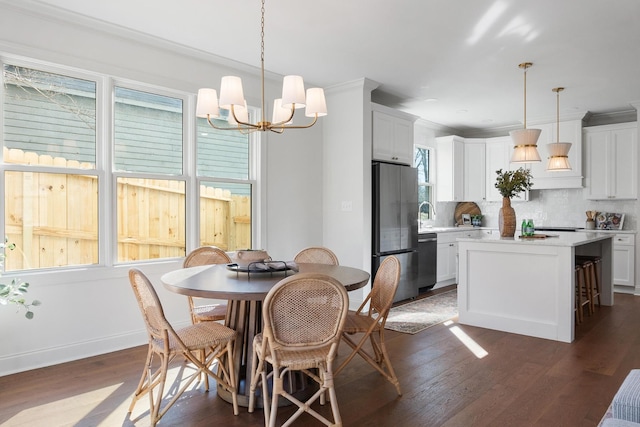 dining room with dark wood-type flooring, sink, crown molding, and an inviting chandelier