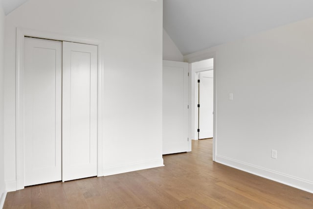 unfurnished bedroom featuring lofted ceiling, a closet, baseboards, and wood finished floors