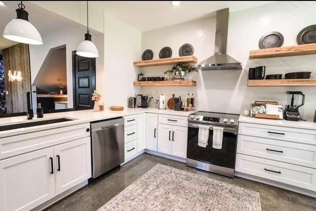 kitchen featuring white cabinets, decorative light fixtures, wall chimney range hood, stainless steel appliances, and sink