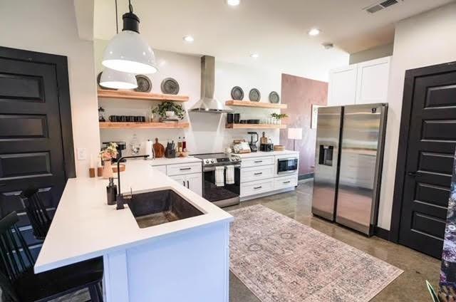 kitchen featuring pendant lighting, appliances with stainless steel finishes, island exhaust hood, kitchen peninsula, and a breakfast bar