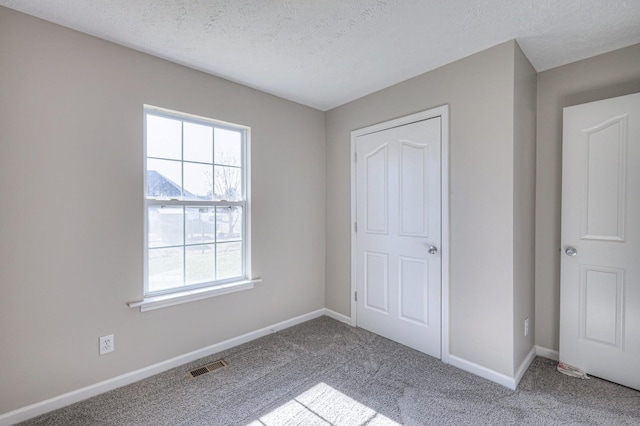 unfurnished bedroom featuring light colored carpet, a textured ceiling, and a closet