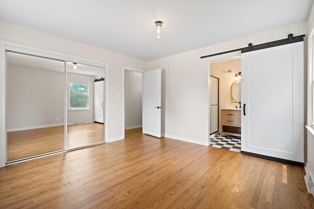 unfurnished bedroom featuring connected bathroom, a closet, light hardwood / wood-style floors, and a barn door