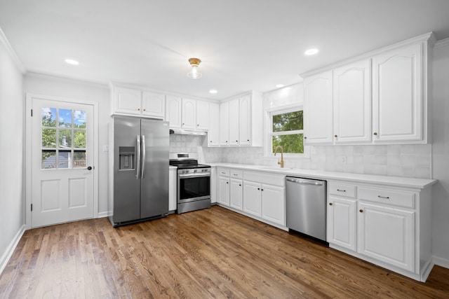 kitchen featuring stainless steel appliances, a healthy amount of sunlight, backsplash, white cabinets, and light hardwood / wood-style flooring