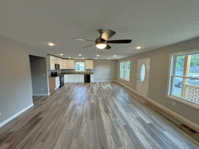 unfurnished living room with ceiling fan, a textured ceiling, and light hardwood / wood-style floors