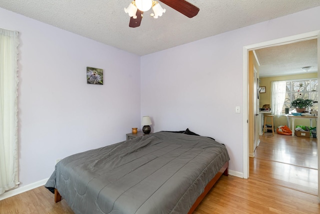 bedroom featuring a ceiling fan, a textured ceiling, baseboards, and wood finished floors