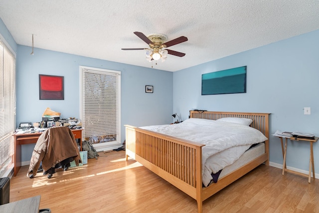 bedroom with ceiling fan, a textured ceiling, baseboards, and wood finished floors