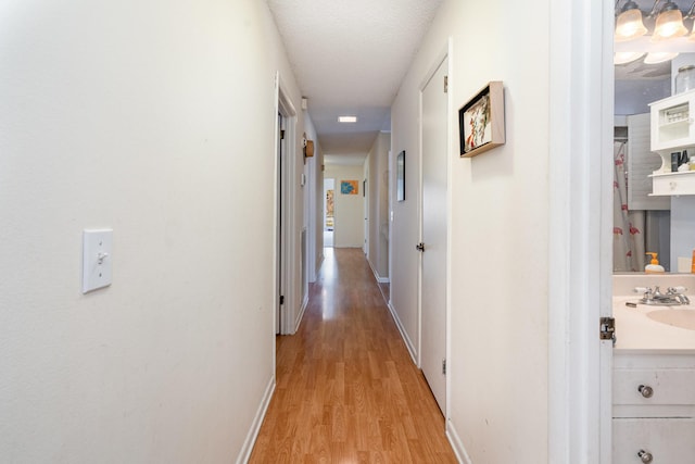 hallway with light wood-style floors, a sink, and baseboards