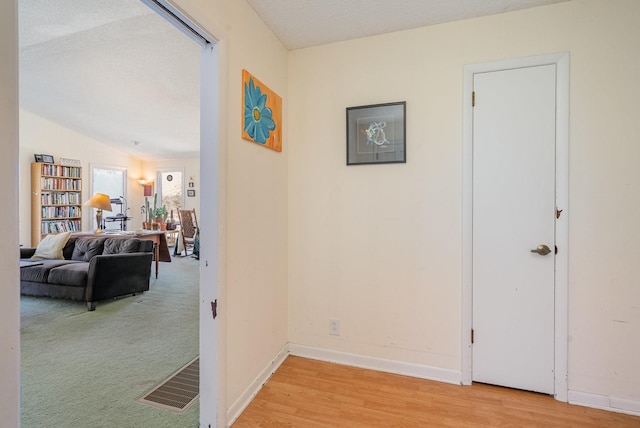 hallway with baseboards, visible vents, wood finished floors, carpet, and a textured ceiling