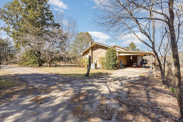 view of home's exterior with driveway, a carport, a chimney, and central air condition unit