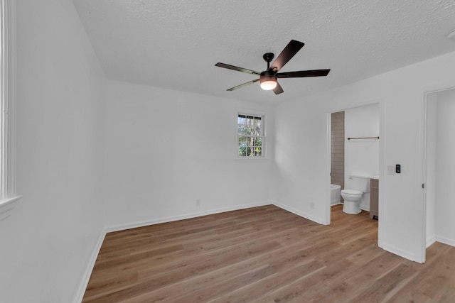 unfurnished bedroom featuring ceiling fan, a textured ceiling, ensuite bathroom, and light hardwood / wood-style flooring