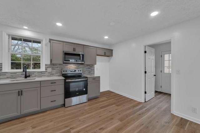 kitchen featuring sink, light hardwood / wood-style flooring, appliances with stainless steel finishes, plenty of natural light, and gray cabinetry