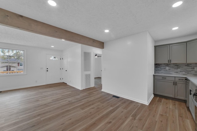 interior space with light wood-type flooring, gray cabinetry, beam ceiling, and tasteful backsplash