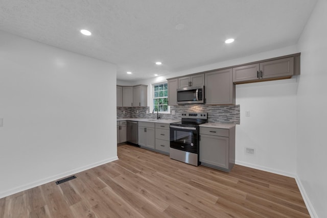 kitchen with gray cabinets, stainless steel appliances, tasteful backsplash, light hardwood / wood-style flooring, and sink