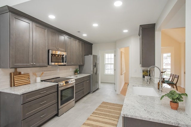 kitchen featuring light stone counters, sink, appliances with stainless steel finishes, and dark brown cabinets