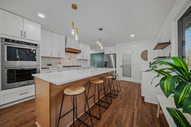 kitchen with stainless steel appliances, a center island with sink, and white cabinets