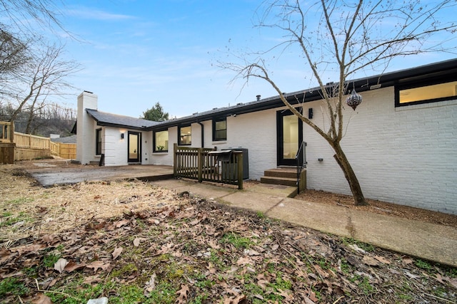 rear view of property with brick siding, a patio, a chimney, entry steps, and fence