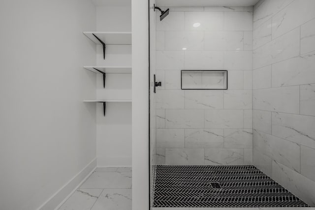 bathroom featuring marble finish floor, a shower stall, and baseboards