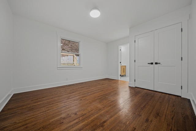 unfurnished bedroom featuring a closet, visible vents, dark wood finished floors, and baseboards