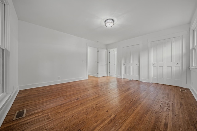 unfurnished bedroom with baseboards, wood finished floors, visible vents, and multiple closets