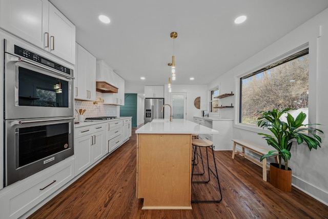 kitchen featuring a breakfast bar, stainless steel appliances, light countertops, white cabinets, and an island with sink