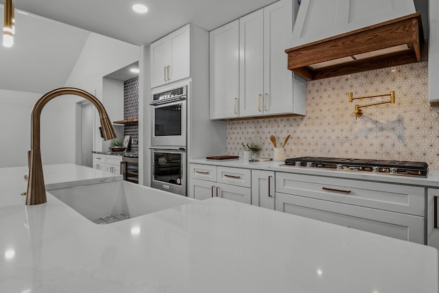 kitchen with tasteful backsplash, custom range hood, appliances with stainless steel finishes, white cabinetry, and a sink