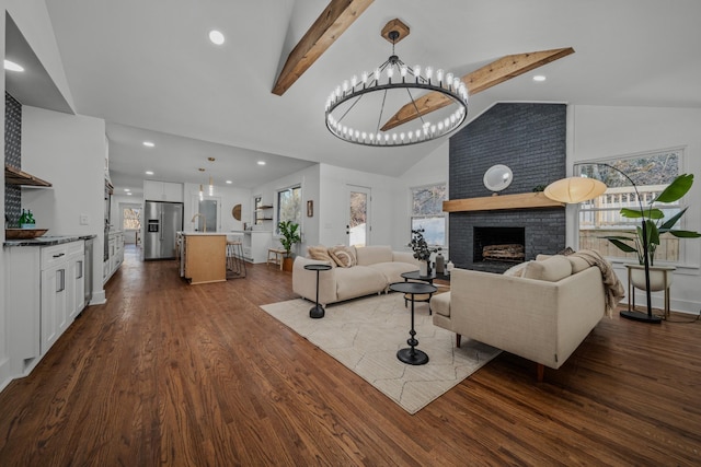 living room with wood finished floors, an inviting chandelier, a brick fireplace, beam ceiling, and recessed lighting