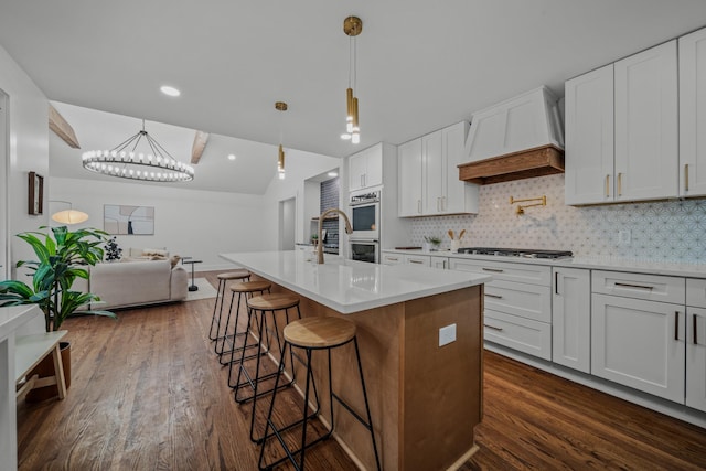 kitchen featuring white cabinetry, a kitchen island with sink, custom exhaust hood, and light countertops