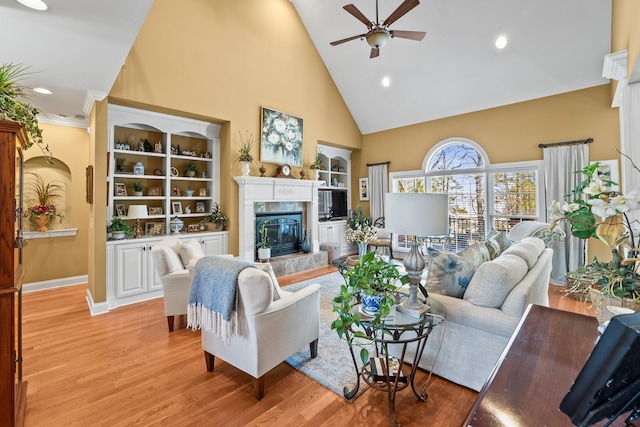 living room featuring ceiling fan, built in features, a fireplace, high vaulted ceiling, and light hardwood / wood-style flooring