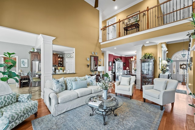 living room with crown molding, a towering ceiling, wood-type flooring, and decorative columns