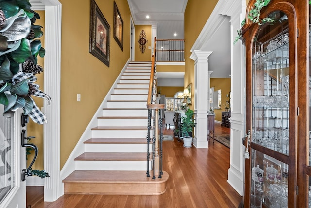 foyer entrance featuring wood-type flooring, ornamental molding, and ornate columns