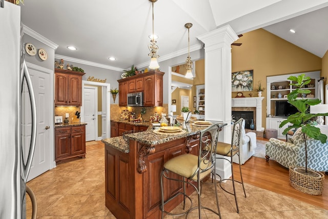 kitchen with appliances with stainless steel finishes, lofted ceiling, a kitchen bar, and decorative columns