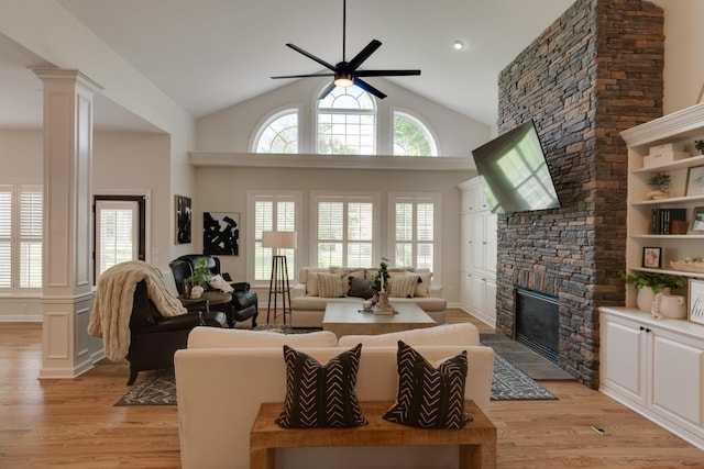 living room with ceiling fan, vaulted ceiling, a stone fireplace, and light hardwood / wood-style flooring