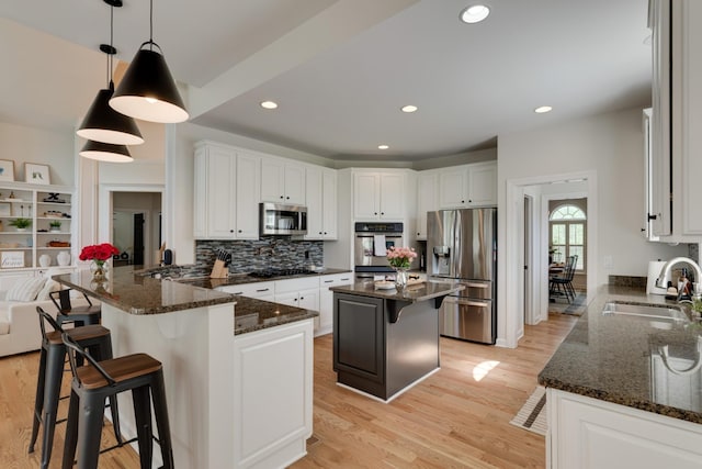 kitchen with kitchen peninsula, stainless steel appliances, dark stone counters, hanging light fixtures, and sink