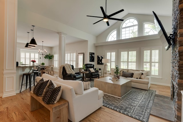 living room with light wood-type flooring, ornate columns, and ceiling fan with notable chandelier