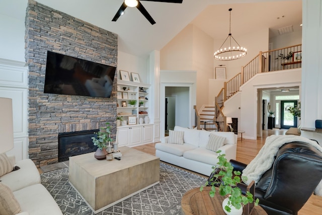 living room featuring a fireplace, hardwood / wood-style floors, high vaulted ceiling, built in shelves, and ceiling fan with notable chandelier