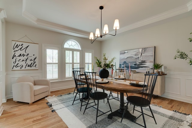 dining space featuring light wood-type flooring, a chandelier, crown molding, and a raised ceiling