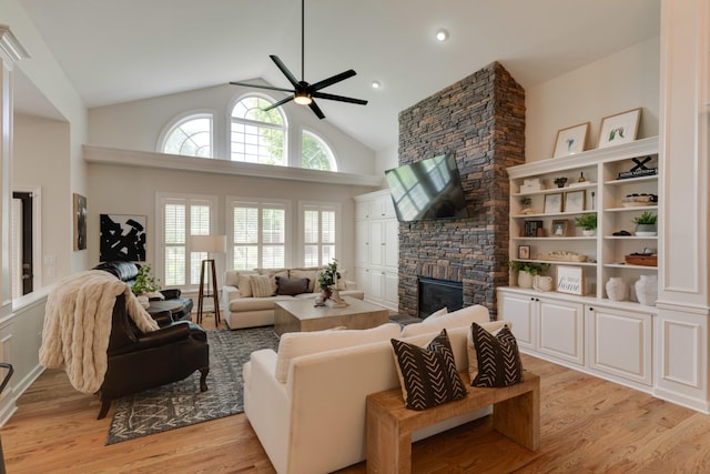 living room featuring ceiling fan, high vaulted ceiling, a stone fireplace, and light hardwood / wood-style floors