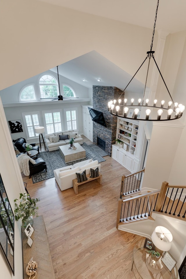 living room featuring high vaulted ceiling, a stone fireplace, a chandelier, and light hardwood / wood-style flooring