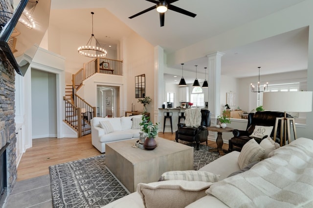 living room with a high ceiling, light wood-type flooring, a fireplace, and ceiling fan with notable chandelier