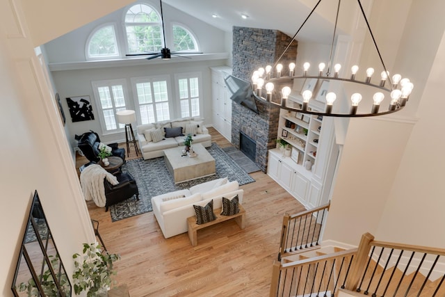 living room with a fireplace, ceiling fan with notable chandelier, light hardwood / wood-style flooring, and high vaulted ceiling