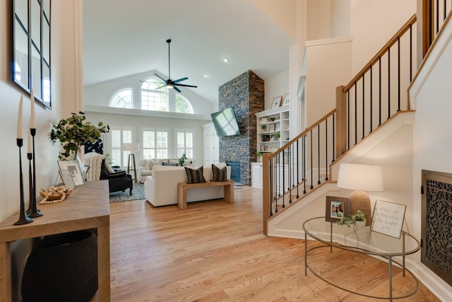 living room with light hardwood / wood-style floors, high vaulted ceiling, ceiling fan, and a fireplace